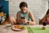 A teenage girl sits with a meal on a plate in front of her but is distracted and looking at her phone