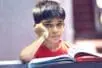 A young boy sits over an open book with his hand on his face