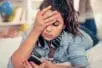 A young woman puts her hand to her head and looks at her phone