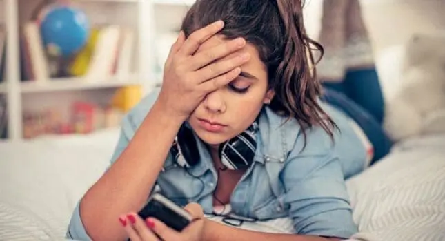 A young woman puts her hand to her head and looks at her phone