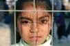 A girl looks at the camera from behind a fence