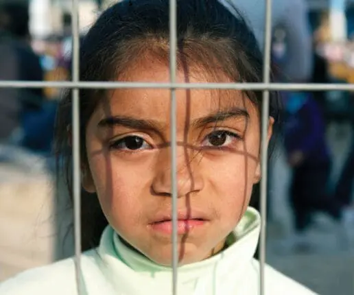 A girl looks at the camera from behind a fence