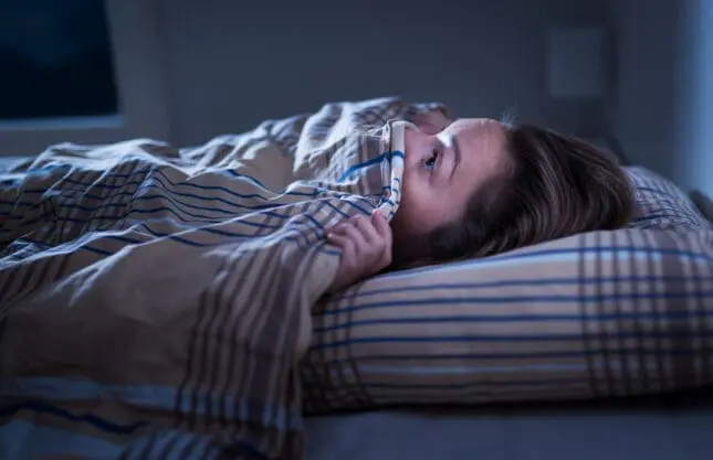 A young girl hides under her covers