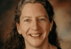 Woman smiling against a dark background.