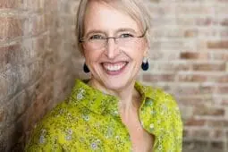 Woman in green shirt against brick backdrop smiling