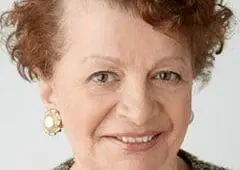 Woman with short red hair and pearl earrings smiling.