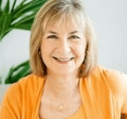 Woman in front of plant in orange sweater smiling