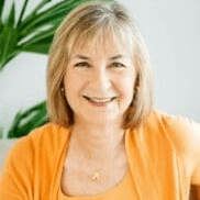 Woman in front of plant in orange sweater smiling