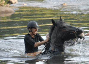 A woman sits joyfully on a horse emerging from water
