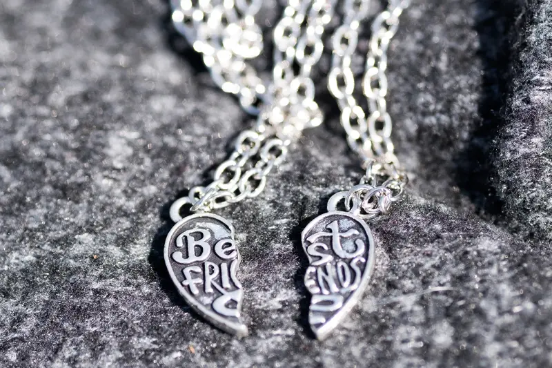 A two-piece friendship necklace rests on a stone backdrop