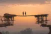 Two figures stand atop a newly constructed bridge facing the horizon