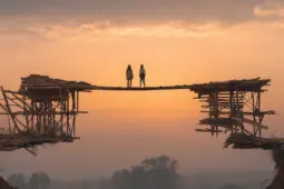 Two figures stand atop a newly constructed bridge facing the horizon