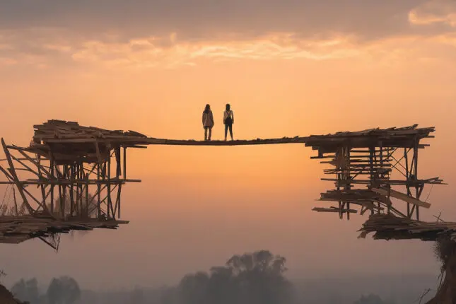 Two figures stand atop a newly constructed bridge facing the horizon