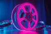 A neon film reel sits and glows