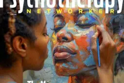 A woman holds a paintbrush, painting in her own face