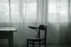 An empty chair sits in front of windows covered in light fabric