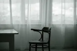 An empty chair sits in front of windows covered in light fabric
