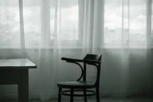 An empty chair sits in front of windows covered in light fabric