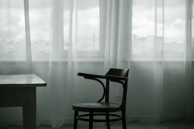 An empty chair sits in front of windows covered in light fabric