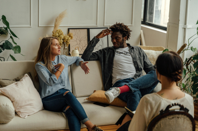 A couple sits on a couch during a therapy session talking intently