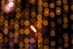 A single candle burns in the center of the image with a glowing gold background