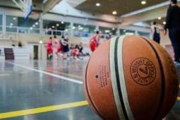 A basketball on a court with players in the background | Photo by Bk Aguilar/Pexels