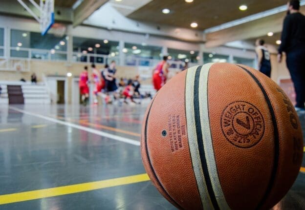 A basketball on a court with players in the background | Photo by Bk Aguilar/Pexels