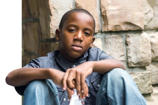 A young Black boy sitting with his arms on his knees