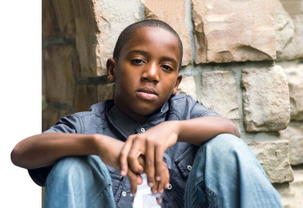 A young Black boy sitting with his arms on his knees