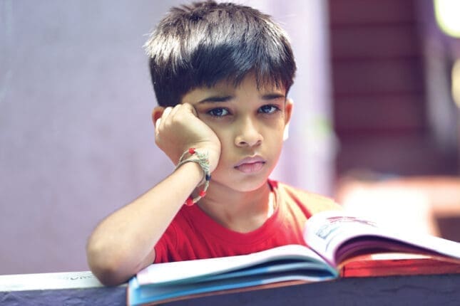 A young boy sits over an open book with his hand on his face