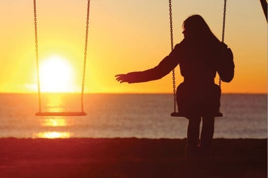 A woman on a swing reaches a hand out to the empty swing next to her