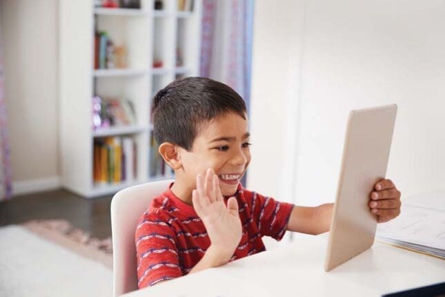 A young boy waves to a tablet screen