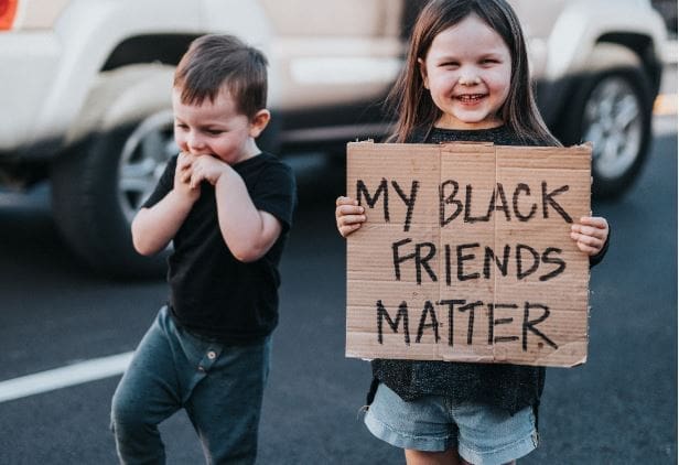 A young girl holds a sign that reads "My Black Friends Matter"