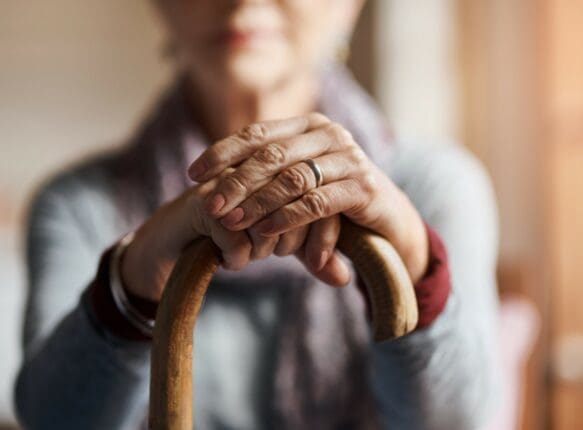 An older woman rests her hands on a cane