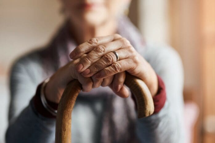 An older woman rests her hands on a cane