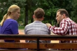 Two parents sit on a bench with their teen