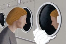 A woman looks at her reflection in a laundry machine window