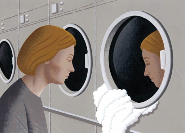 A woman looks at her reflection in a laundry machine window