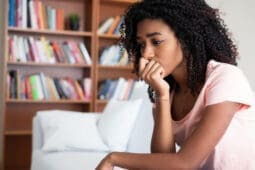 A Black woman sits with her hand on her chin