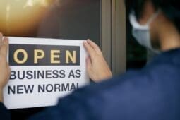 A person puts up a sign that reads "Open: Business as New Normal"