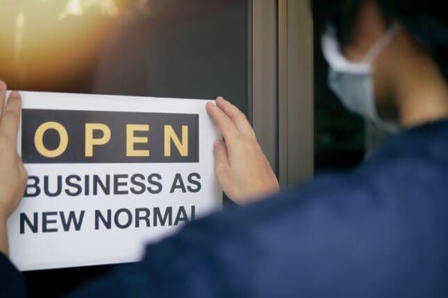 A person puts up a sign that reads "Open: Business as New Normal"