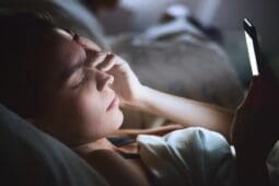 A woman awake in bed looks at her phone