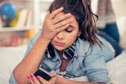 A young woman puts her hand to her head and looks at her phone