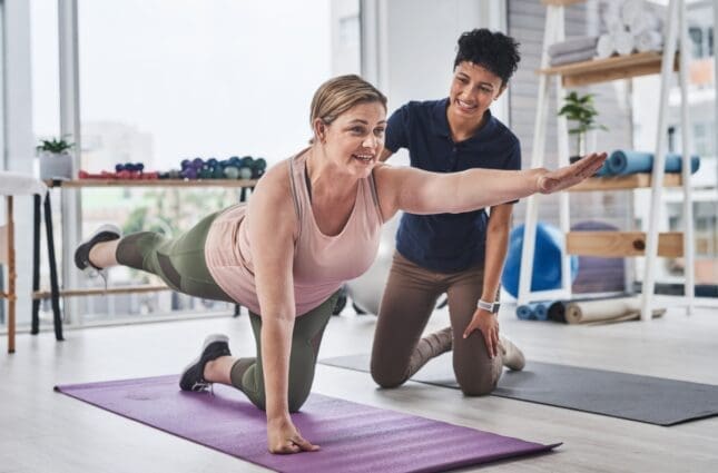 A yoga trainer helps a woman with a pose