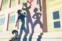 A young boy approaches his school as shadows of threatening figures appear before him