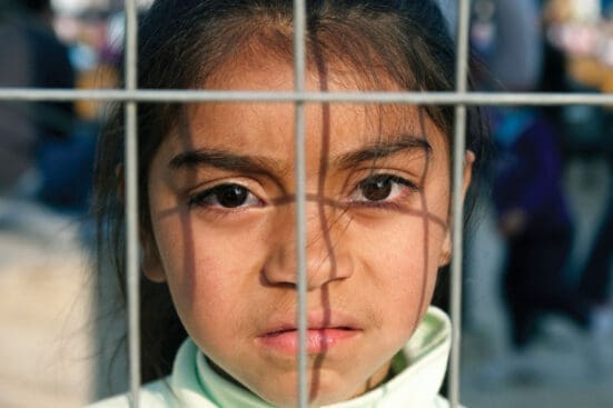 A girl looks at the camera from behind a fence