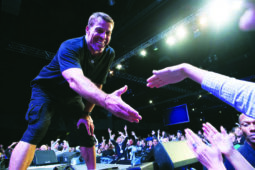 A man on stage holds his hand out to someone in the crowd