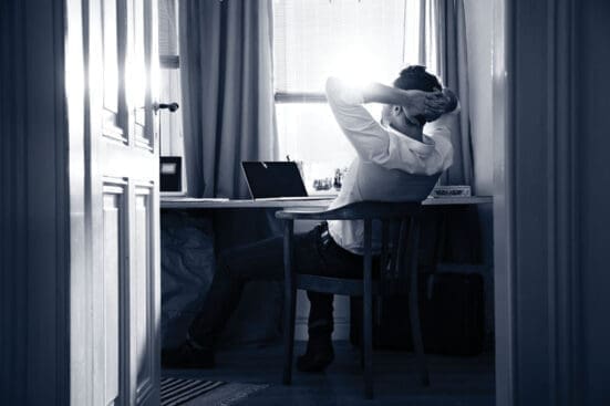 A man at a desk leans back with his head resting in his hands