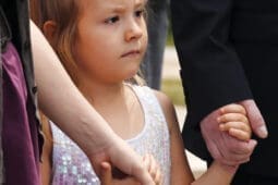 A young child holds hands with two adults