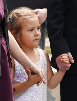 A young child holds hands with two adults